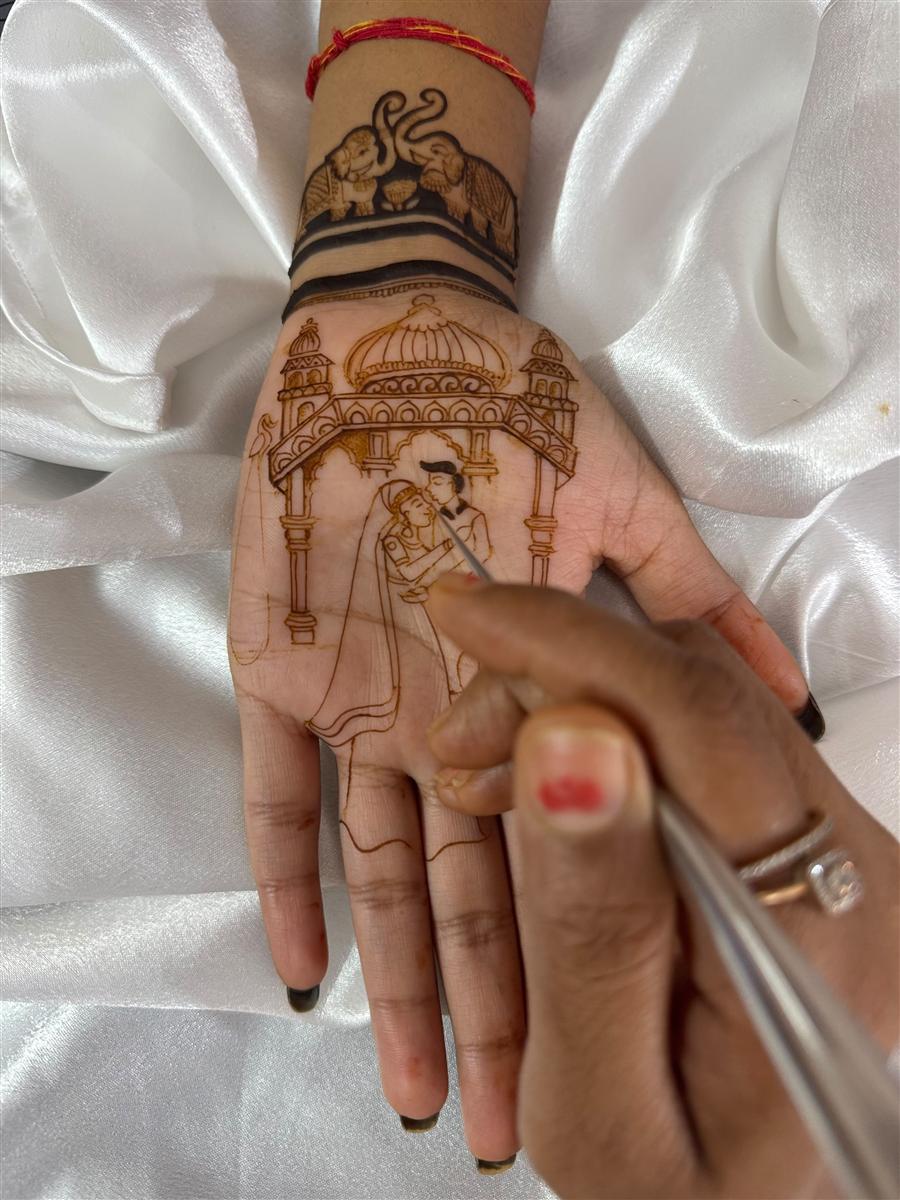 Hands sketching a couple under a palace dome in henna